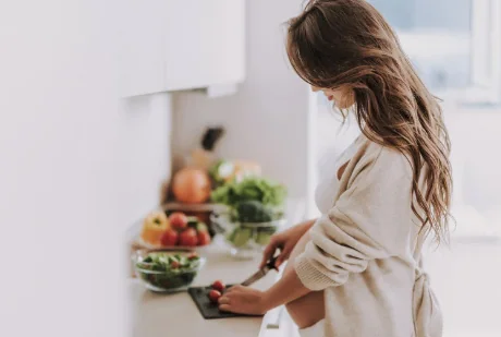 Pregnant woman chopping fresh vegetables in a bright kitchen